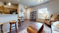 This single-floor home offers a thoughtfully designed layout that balances comfort and style. The open-concept living area is immediately welcoming, featuring rich hardwood-style flooring, vaulted ceilings with a ceiling fan, and generous natural light streaming through plantation-shuttered windows. A bold patterned accent chair, a sculptural solid-wood coffee table, and a neutral sofa anchored by a layered area rug create an inviting and well-curated gathering space. Leaning ladder shelves add decorative storage, while wall art and metallic accents contribute to the warm, eclectic aesthetic.

The kitchen is efficiently designed with dark espresso cabinetry, granite-style countertops, and full black appliance suite including a range, dishwasher, and microwave. A breakfast bar with bar seating connects the kitchen to the living space, making it ideal for both casual dining and entertaining.

The bedroom is a serene retreat, centered around a stately dark-wood bed frame and complemented by soft carpeting, matching nightstands, and ample natural light. A walk-in closet and additional closet storage provide excellent organization.

The full bathroom echoes the kitchen's design language with matching dark cabinetry, granite countertops, a single vanity, and a tub-shower combination. Consistent wood-look flooring and neutral tones unify the entire space.
