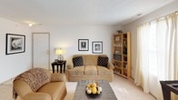 This single-floor residence offers a thoughtfully arranged layout with a neutral color palette, soft carpeting throughout the main living areas, and tile flooring in the kitchen and bathrooms. The living room serves as a welcoming entry point, featuring a textured ceiling, a tiled entryway, and ample space for seating arrangements. Natural light filters in through curtained windows, creating a bright and comfortable atmosphere.

The kitchen is efficiently designed with light wood cabinetry, ample counter space, and a full suite of appliances including an electric range, refrigerator, microwave, and dishwasher. A striped area rug adds a decorative touch to the light tile floor. The kitchen opens directly into the dining area, which benefits from a large sliding glass door that floods the space with natural light and provides an outdoor view.

The residence includes two carpeted bedrooms, each offering closet storage and windows with natural light. The primary bedroom features a sliding closet door and wall art, while the second bedroom includes a window treatment providing privacy.

Two bathrooms complete the layout — one featuring a vanity with dual mirrors and ample cabinetry, and the other with a full tub-shower combination, toilet, and understated finishes throughout.