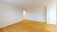 Located at 214 Price Ave in the welcoming borough of Narberth, PA, this single-floor unit offers a well-organized layout that makes efficient use of its compact footprint. The entry hallway leads through a distinctive arched doorway, setting a classic architectural tone that continues throughout the space. Warm-toned hardwood floors run through the main living area and hallway, adding character and continuity.

The combined kitchen and living room serves as the heart of the unit. The living area benefits from natural light streaming through double windows dressed with horizontal blinds, and a ceiling fan provides year-round comfort. A radiator unit along the wall provides reliable heating. The galley-style kitchen is thoughtfully designed with ample warm wood cabinetry lining both sides, a white refrigerator, gas range, microwave, and light-toned countertops. A window above the sink allows for additional natural light and ventilation.

A decorative arched niche adds an elegant architectural accent to the living room walls. The bathroom features a full tub-shower combination with white tile surround and a louvered window for natural ventilation. A closet provides convenient storage. The overall palette of neutral, warm beige tones throughout creates a cohesive and inviting atmosphere, well-suited to comfortable everyday living in a charming suburban setting.