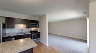 This single-floor residence offers a functional and cohesive layout connecting the kitchen, dining, and living areas. The kitchen is outfitted with dark espresso cabinetry, granite countertops, and a full suite of stainless steel appliances including a refrigerator, range, microwave, and dishwasher. A peninsula with additional granite counter space provides extra prep area and serves as a natural divider between the kitchen and the adjoining living space.

The living area is generously proportioned, finished with neutral-toned carpet, and features a sliding glass door that opens to a private balcony with outdoor views, allowing natural light to fill the space. A secondary window further enhances brightness in the room.

The bedrooms are carpeted and finished in warm neutral tones. Each room includes a closet with louvered bifold doors, providing organized storage. One bedroom features an angled ceiling detail, adding architectural interest to the space.

The bathroom includes tile flooring, a wood-toned vanity with storage, and clean, neutral wall finishes. Throughout the unit, consistent use of light beige tones and white trim creates a cohesive, move-in-ready aesthetic.