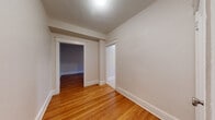 This single-floor residence offers a clean, classic interior defined by warm-toned hardwood floors that run throughout the living areas and bedrooms, complemented by crisp white baseboards and trim that lend a timeless character to the space. The layout is thoughtfully organized, with multiple rooms connected by doorways featuring traditional door casings that add architectural detail throughout.

The living area is generously proportioned, bathed in natural light from large windows that frame views of surrounding greenery. Each bedroom is well-sized, with hardwood floors continuing seamlessly from room to room. Radiator heating is present in at least one bedroom, reflecting the home's enduring, period-appropriate infrastructure. An air conditioning unit installed in a window ensures year-round comfort.

The bathroom is finished in a clean, all-white palette with classic subway tile wainscoting, mosaic tile flooring, a vanity with under-sink storage, and a bright window that keeps the room feeling fresh and airy.

The kitchen features warm wood cabinetry, a full suite of white appliances including a refrigerator and electric range, and a window overlooking the outdoors. Light tile flooring completes the practical and functional design. Throughout the space, neutral wall tones and consistent finishes create a cohesive, inviting atmosphere.