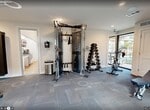 Located at 320 East Wintergreen Road in DeSoto, Texas, this 440-square-foot fitness center offers a compact yet well-equipped workout facility on a single floor. The space features clean white walls, recessed lighting, and durable carpet tile flooring designed to withstand heavy equipment and high foot traffic. Natural light fills the room through multiple large windows and glass doors, providing views of the surrounding outdoor areas and creating an open, energizing atmosphere. The cardio zone is anchored by two treadmills and an elliptical trainer positioned near the windows. The strength training area includes a Matrix functional trainer cable machine, a dumbbell rack with a full set of weights, a weight bench, and a seated strength machine, offering a well-rounded selection for resistance workouts. A wall-mounted flat-screen television is positioned for visibility across the floor, enhancing the workout experience. Glass doors along one wall provide direct outdoor access, further contributing to the room's sense of openness. Fitness center rules are posted on the wall for user reference. The overall design is modern and functional, reflecting a thoughtfully organized community amenity space suitable for a variety of fitness routines.
