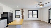 Located at 511 Maple Blvd in Kansas City, Missouri, this one-bedroom, one-bathroom unit offers a well-organized single-floor layout with a clean, modern aesthetic. Light wood-style vinyl flooring runs throughout the space, complementing the bright white walls and creating a cohesive, contemporary feel.

The combined kitchen and living area forms the heart of the unit. The kitchen is equipped with gray cabinetry, dark countertops, and a full suite of black appliances — including a gas range, dishwasher, over-the-range microwave, and refrigerator. A freestanding island with a butcher-block top provides additional prep and dining space. The living area is bathed in natural light through bold black-framed windows fitted with blinds, and a ceiling fan adds comfort and airflow.

The bedroom is a cozy, private retreat featuring its own black-framed window with an outdoor view and baseboard heating. A dedicated laundry area accommodates an in-unit washer, adding everyday convenience.

The bathroom is finished with wood-look flooring, a walk-in shower with white surround panels, and a floating wood-toned vanity with a black faucet and mirror. Exposed brick detailing in the living area adds a touch of character and warmth to this otherwise clean, modern space.