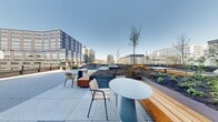The Basecamp Deck at 757 Thomas Street is a thoughtfully designed rooftop outdoor amenity space situated in Seattle's vibrant South Lake Union neighborhood. The deck is divided into several distinct zones, each offering a unique setting for gathering, relaxing, or taking in the surroundings. A spacious hardscape terrace features modern round bistro tables paired with slatted wood-and-metal chairs, ideal for casual seating or informal meetings. Adjacent to this area, raised planted garden beds add greenery and natural texture to the urban environment, accented by young trees that provide a touch of nature amid the cityscape. A lounge area is furnished with solid wood-framed outdoor sofas and armchairs upholstered in muted green tones, centered around a sculptural side table, creating an inviting setting for conversation. A turf lawn area provides open, flexible space and incorporates a distinctive tiered wood platform stage, suitable for small gatherings or performances. Glass panel railings along the perimeter ensure unobstructed panoramic views of the Seattle skyline, including a direct sightline to the Space Needle. The deck connects to the building's glass curtain wall façade, reinforcing a clean, contemporary aesthetic throughout. Abundant natural light and open sky views define the overall atmosphere of this well-appointed outdoor space.