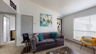 This single-floor unit at Mainstream Apartments offers a thoughtfully designed layout that balances comfort and functionality. The living room serves as the heart of the home, featuring plush carpeting, soft neutral walls, and a bright window that allows natural light to fill the space. Colorful wall art adds a welcoming touch to the relaxed, open atmosphere.

Adjacent to the living area, the dining space features wood-look vinyl flooring and room for a full dining set, creating a natural transition between living and kitchen areas. The galley-style kitchen is efficiently organized with gray cabinetry, black appliances including a refrigerator and range, and hard-surface countertops, all set atop durable wood-look flooring.

The unit includes two carpeted bedrooms, each with windows that bring in natural light. The primary bedroom offers a serene and restful atmosphere with ample space, while the second bedroom features a ceiling fan and generous floor area. A shared bathroom includes a wide vanity with a speckled countertop, an integrated sink, a dark-framed mirror, and wood-look flooring, offering a clean and modern aesthetic throughout.