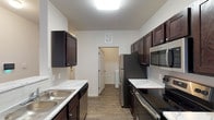This single-floor residence offers a well-organized layout with distinct living, sleeping, and utility spaces. The galley-style kitchen is a functional centerpiece, featuring rich dark-espresso cabinetry, marble-patterned countertops, stainless steel appliances including a refrigerator, electric range, microwave, and dishwasher, and a double stainless steel sink. Wood-look plank flooring runs throughout the kitchen and connects seamlessly to the open living area. The spacious living room benefits from multiple windows fitted with horizontal blinds, allowing natural light to fill the space, and flows directly from the kitchen's peninsula-style pass-through.

The bedrooms are finished with plush neutral carpet and ceiling fans, providing a comfortable retreat. One bedroom features a large window offering natural light, while another includes access to a closet and connecting hallway. The bathroom is equipped with a soaking tub and shower combo, dark cabinetry with marble-patterned countertops, and wood-look tile flooring. A dedicated in-unit laundry room with wire shelving accommodates a full-sized washer and dryer, adding everyday convenience. The overall aesthetic is clean and contemporary throughout.