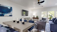 Located at 315 N Associated Rd in Brea, California, this single-floor community amenity space offers a thoughtfully designed layout encompassing a combined kitchen and living room, a dedicated exercise room, and a hallway connecting the areas. The open-concept kitchen and living room is bright and contemporary, featuring light wood-tone cabinetry, white quartz countertops, stainless steel appliances, and large windows that frame views of the surrounding mature trees, flooding the space with natural light. Light hardwood-style flooring runs throughout, complementing the clean, neutral color palette. The living and dining area is stylishly appointed with a wall-mounted flat-screen TV, a sleek credenza, bold blue accent chairs and dining seats, and abstract artwork that adds a modern flair. A ceiling fan with a modern matte-black finish adds both function and style overhead. The exercise room is a standout feature, boasting soaring vaulted ceilings with exposed beam detailing, expansive clerestory windows that bring in abundant natural light, floor-to-ceiling mirrors, and a robust selection of fitness equipment including treadmills, ellipticals, cable machines, and strength-training stations—all set on durable rubber flooring. Together, these spaces create a versatile and well-equipped community facility.