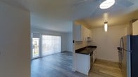 This 2-bedroom, 1-bathroom residence is thoughtfully laid out across a single floor, offering a comfortable and functional living environment with modern finishes throughout. The open-concept design seamlessly connects the kitchen and living area, creating a spacious, airy feel. The kitchen features crisp white cabinetry, dark countertops, a stainless steel sink, and pendant lighting, providing both style and practicality. Light wood-style flooring runs throughout the main living area, adding warmth and continuity to the space. The living room is bathed in natural light, courtesy of large sliding glass doors fitted with vertical blinds that lead directly to an outdoor area, making the transition between indoor and outdoor living effortless. The neutral white walls and light-toned ceiling contribute to the clean, contemporary aesthetic of the home. The layout is designed to maximize usable space, ensuring each area serves a clear and practical purpose. Overall, the residence strikes a balance between modern design and everyday comfort, making it a well-appointed and move-in ready home.