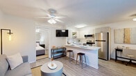 Located at 3525 SW 24th Ave in Gainesville, FL, this well-designed one-bedroom, one-bathroom unit maximizes every square foot with a thoughtful, open-concept layout. The combined kitchen and living area serves as the heart of the home, anchored by light wood-style flooring that runs throughout. The kitchen is outfitted with stainless steel appliances—including a refrigerator, electric range, and built-in microwave—complemented by white cabinetry, open shelving, and a light-colored countertop peninsula that doubles as a breakfast bar with barstool seating. The living area benefits from a ceiling fan, a window that brings in natural light, and enough room for a comfortable seating arrangement. The bedroom is a calm, neutral retreat featuring a ceiling fan, wood-style flooring, and a closet for storage. The bathroom includes a full tub-shower combination with tiled surround, a single-sink vanity with white cabinetry, and a wood-framed mirror. Throughout the unit, a clean, neutral color palette with white walls and warm flooring tones creates a bright and cohesive ambiance well-suited for comfortable everyday living.