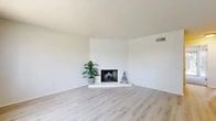 Located at 235 W Orangewood Ave in Anaheim, CA, this well-appointed 2-bedroom, 2-bathroom single-floor residence offers a thoughtfully designed layout with a bright, neutral aesthetic throughout. The living room serves as the heart of the home, featuring light wood-look flooring, a textured ceiling, and a striking corner fireplace clad in white-painted brick — a standout architectural detail that anchors the space. A large window with vertical blinds fills the room with natural light, creating an open and airy atmosphere. The kitchen and living area share a connected layout, enhancing the flow of the space. Both bedrooms are carpeted and finished in soft neutral tones, with ceiling fans adding comfort and practicality. The primary bedroom offers a generous footprint with ample room for furnishings. A dedicated closet with built-in upper cabinetry and shelving provides organized storage. The two bathrooms are finished in clean whites, each featuring light wood-look flooring, white vanities with stone-look countertops, and brushed nickel fixtures. One bathroom includes a full tub-shower combination. The floorplan model reveals access to an outdoor area with mature greenery. The overall design is clean, cohesive, and move-in ready.