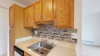 This single-floor space offers a practical and comfortable layout designed for everyday living. The floor plan reveals a series of well-connected rooms that flow naturally from one to the next, creating a cohesive and livable environment throughout.

The kitchen is a standout feature, showcasing warm honey-toned oak cabinetry with sleek bar-pull hardware. A decorative mosaic tile backsplash in neutral tones of gray, beige, and brown adds a stylish focal point between the upper and lower cabinets. Light countertops provide ample workspace, and a stainless steel sink completes the functional setup.

Adjacent living areas are finished with light-toned flooring and neutral wall colors, contributing to a bright and airy atmosphere. Large windows allow natural light to filter in throughout the space, enhancing the open feel of the rooms. The layout includes distinct zones that appear suited for dining and relaxation, each clearly defined within the overall floor plan.

The design emphasizes clean lines and a neutral color palette, making the space versatile and easy to personalize. Overall, this single-floor property offers a well-balanced combination of functional design and comfortable living spaces, well-suited for a variety of lifestyles.