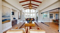 Located in Willowbrook, IL, this single-floor community clubhouse offers a generously proportioned layout designed for both relaxation and activity. The centerpiece is a stunning great room distinguished by soaring vaulted ceilings adorned with exposed wood beams and an elegant chandelier. A dramatic wall of floor-to-ceiling windows floods the space with natural light and frames outdoor views, creating an open, airy ambiance. Wide-plank hardwood flooring runs throughout, tying the areas together cohesively. A built-in wet bar with herringbone tile detailing and custom cabinetry provides a refined focal point in this main gathering space. The adjoining living room features a full-height stacked stone fireplace with a mounted television, complemented by warm neutral tones and ample seating. The combined dining and lounge area transitions naturally from the living spaces, offering multiple seating arrangements bathed in natural light from a row of windows, with curated artwork accenting the walls. The exercise room is fully equipped with treadmills, a rowing machine, stability balls, and mirrored walls, featuring bold navy and gold accent stripes that energize the space. A ceiling fan and skylights keep the room well-ventilated and bright. Together, these spaces form a thoughtfully designed, versatile facility ideal for community gatherings and wellness activities.
