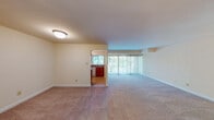 This single-floor residence offers a thoughtfully laid-out living space with a clean, neutral aesthetic throughout. The expansive living room is carpeted and bathed in natural light from a large sliding glass door fitted with vertical blinds, offering views of lush greenery outside. The open feel of the living area is enhanced by its generous proportions and seamless connection to the kitchen through a wide pass-through opening.

The kitchen is efficiently designed with warm wood cabinetry, dark laminate countertops, and tile flooring. It is equipped with a gas range, dishwasher, and a full-size refrigerator, along with a window that brings in additional natural light.

The bedroom is spacious and carpeted, featuring two separate closets — both with bifold doors — providing ample storage. An attached bathroom is accessible directly from the bedroom, while a second full bathroom serves the rest of the unit. Both bathrooms are finished with warm-toned tile flooring, wood vanity cabinetry, white countertops, framed mirrors, and a full tub-shower combination with white subway tile surround.

Additional interior space is visible in the floor plan, suggesting a versatile bonus or secondary room. The overall palette of warm beige and cream tones creates a bright, welcoming ambiance throughout the home.