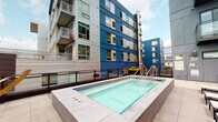 Located at 1300 W Lake St in Minneapolis's vibrant Uptown neighborhood, this outdoor amenity deck offers a well-appointed retreat above the city. The centerpiece of the space is a sleek lap pool finished with blue tile accents and surrounded by large-format light stone pavers. A generous arrangement of modern chaise lounges lines the poolside, providing ample space for sunbathing and relaxation, while colorful planters filled with seasonal blooms add a lively touch of greenery along the perimeter.

A dedicated lounge zone features a sturdy pergola structure fitted with a slatted shade canopy, string lights, and outdoor speakers, creating an inviting covered gathering space. Beneath the pergola, a freestanding hammock with a cushioned lounger, along with seating and dining furniture, offer comfortable spots to unwind. The open-air design allows for sweeping views of the surrounding Minneapolis skyline and neighboring architecture.

The deck's contemporary aesthetic is complemented by the bold blue and silver facade of the building itself, which frames the space on multiple sides. Overall, the amenity deck combines functional recreation and relaxed outdoor living in a thoughtfully designed urban setting.