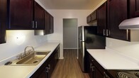 This single-floor residence offers a functional and comfortable layout designed for everyday living. The open living and dining area is finished with durable wood-look flooring and neutral-toned walls, creating a warm and inviting atmosphere. A ceiling fan adds both style and practicality overhead, while large windows fitted with vertical blinds flood the space with natural light. An adjacent storage area with built-in shelving provides convenient organization options.

The galley-style kitchen features rich, dark espresso cabinetry lining both walls, offering generous storage and counter space. Light-toned countertops provide a striking contrast, and stainless steel appliances, including a refrigerator, complete the well-equipped space.

The bedroom is carpeted for comfort and includes a dedicated walk-in closet, offering ample storage. A window with vertical blinds brings in natural light, keeping the room bright and airy.

The full bathroom is thoughtfully appointed with dark cabinetry beneath a wide white vanity countertop, a large mirror, and contemporary overhead lighting. A combined tub and shower with tiled surround and a chrome towel bar round out the space.

A dedicated in-unit laundry room with side-by-side washer and dryer and overhead shelving adds a highly practical convenience to this well-rounded home.
