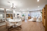Located at 74 Hauppauge Rd in Commack, NY, this single-floor home offers a well-appointed layout that balances modern elegance with everyday functionality. Light hardwood flooring flows throughout the main living areas, lending warmth and continuity to the space. The open-concept living room is bright and inviting, with large windows dressed in sheer linen curtains that allow natural light to filter in, complemented by recessed lighting and curated wall art. The adjacent dining area features vaulted ceiling details, a statement chandelier, gold-framed mirrors, and a classic round dining table — creating a refined yet welcoming atmosphere. The kitchen is outfitted with crisp white shaker cabinetry, quartz countertops, stainless steel appliances with matte black hardware, and a sliding glass door that opens to an outdoor patio. The generously sized primary bedroom offers natural light through a large window and direct access to a walk-in closet with built-in wire shelving. Four bathrooms are finished with marble-look tile flooring, white vanities, and matte black fixtures — exuding a clean, spa-like aesthetic. A dedicated laundry room with side-by-side Samsung washer and dryer rounds out this well-designed home.