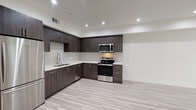 This single-floor residence showcases a thoughtfully designed contemporary interior with a cohesive aesthetic carried throughout each room. The kitchen serves as a standout feature, outfitted with rich, dark wood-grain cabinetry extending from floor to ceiling and providing generous storage. Sleek white quartz countertops offer ample workspace, complemented by a deep double-basin sink with a modern pull-down faucet. Stainless steel appliances, including a refrigerator, electric range, over-the-range microwave, and dishwasher, complete the functional and stylish kitchen. Recessed lighting illuminates the open-concept layout, which flows seamlessly from the kitchen into the living area.

The bedroom is bright and well-proportioned, featuring light hardwood-style flooring that continues from the main living spaces, recessed lighting, and a window that invites natural light. A secondary room offers a clean, versatile space with direct access to the kitchen area. The bathroom presents an elegant finish with large-format marble-style tile flooring, an extended vanity with white countertops, a wide mirror, and a glass-enclosed shower, creating a polished, spa-like atmosphere. Throughout the unit, neutral tones and consistent flooring provide a unified, modern feel.