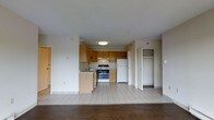 This single-floor residence offers a practical and functional layout centered around an open-concept design that seamlessly connects the kitchen and living areas. The kitchen is outfitted with warm-toned wooden upper cabinetry, a gas range, a full-size refrigerator, and a sink with an adjacent lower cabinet peninsula that defines the space. Light ceramic tile flooring runs throughout the kitchen area, transitioning into rich dark hardwood flooring in the living space, creating a clear and attractive visual distinction between the two zones. The kitchen benefits from flush-mounted ceiling lighting, providing consistent illumination across the workspace. Adjacent to the kitchen, a dedicated closet area with built-in shelving offers convenient storage. The walls are finished in a clean, neutral palette that keeps the interior feeling bright and open. A secondary door visible from the main living area suggests additional rooms or access points within the unit. Overall, the space presents a straightforward and well-organized residential layout with durable finishes and essential amenities thoughtfully arranged for everyday living.