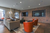 Located at 903 Huff Rd NW in Atlanta's vibrant West Midtown neighborhood, this thoughtfully designed single-floor space seamlessly merges industrial character with contemporary sophistication. The interior is anchored by striking exposed brick accent walls that provide a warm, textural contrast against the crisp white walls and detailed crown molding found throughout.

Distinctive arched black-framed windows are a defining architectural feature, drawing in generous natural light while framing views of the surrounding neighborhood. The floors transition between rich hardwood and polished concrete, adding visual interest and reinforcing the space's dynamic aesthetic.

The main living area is generously proportioned, comfortably accommodating multiple seating zones. A large sectional sofa pairs with vibrant orange swivel accent chairs and a wall-mounted flat-screen television, creating an inviting entertainment hub. An adjacent reading nook benefits from a row of arched windows, making it an ideal retreat filled with natural light.

The open layout extends into a dining area, where a long communal table surrounded by wooden chairs offers ample seating. Recessed lighting throughout ensures the space is well-lit at any hour. Thoughtful transitional columns and well-placed wall art add architectural depth and a curated, polished finish to the overall design. This space offers a compelling blend of character and modern functionality.