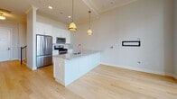 Located at 170 S 6th St in Philadelphia's storied Old City neighborhood, this two-floor residence blends classic architectural character with contemporary interior finishes. The main living level features light-toned hardwood flooring throughout, crown molding, and generous natural light streaming through large multi-pane windows that open to a balcony. Pendant lighting accentuates the open-concept layout, which flows seamlessly from the living area into a well-appointed kitchen. The kitchen is outfitted with white shaker cabinetry, granite countertops, a central island with an undermount sink, stainless steel appliances including a gas range and built-in microwave, and pendant fixtures overhead. A half bath on this level features a sleek pedestal sink with an oval pivot mirror and chrome fixtures, finished with dark tile flooring. The upper floor showcases one of the residence's most distinctive architectural elements: striking arched windows with ornate fan detailing that frame sweeping views of the surrounding cityscape. Carpeted bedrooms on this level are finished with crown molding and offer a quiet, refined ambiance. A full bathroom features a soaking tub with tiled surround and an overhead shower. A decorative wrought iron staircase connects the two levels, reinforcing the home's elegant character throughout.
