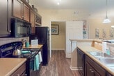 This single-floor unit at Enterprise Way in Maryville, Tennessee offers a thoughtfully designed layout with consistent wood-look flooring flowing throughout. The open living and dining area is finished with crown molding, a ceiling fan, and an arched passageway that draws natural light from a forward-facing window, creating a bright and welcoming atmosphere.

The galley-style kitchen is well-appointed with rich, dark espresso cabinetry extending to the ceiling, light laminate countertops, a tile backsplash, and black appliances including a range, microwave, refrigerator, and dishwasher. Pendant lighting over the breakfast bar adds a functional decorative touch.

The bedrooms feature dark hardwood-style flooring, ceiling fans, and windows fitted with blinds that admit ample natural light, with some offering outdoor views of the surrounding Maryville landscape. Each room provides generous wall space suitable for flexible furnishing arrangements.

Two full bathrooms serve the unit, each outfitted with dark-framed vanity mirrors, espresso-finished cabinetry, light countertops, and a tub-shower combination. The overall palette of warm beige walls and dark flooring lends the unit a cohesive, neutral aesthetic throughout.