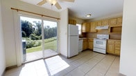Located at 402 Market Dr in Camp Hill, Pennsylvania, this two-floor home offers a functional and well-lit layout. The kitchen is a standout space, finished with large light-colored ceramic tile flooring that reflects natural light throughout the room. Honey-toned wood cabinetry lines the walls, providing ample storage, and is complemented by white appliances including a refrigerator, electric range, and dishwasher. An under-cabinet range hood is positioned above the stove, and a double-basin sink is set beneath a window, allowing natural light into the workspace. A ceiling fan with a light fixture is installed overhead, enhancing air circulation. The most notable feature of the kitchen is a full-size sliding glass door that opens directly to the backyard patio, flooding the space with sunlight and offering unobstructed views of a lush, green lawn bordered by mature trees. This seamless indoor-outdoor connection gives the space a bright, open feel. The overall ambiance of the home is warm and practical, with a suburban setting that emphasizes natural surroundings and comfortable everyday living.