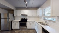 Located at 17105 Gulf Blvd in North Redington Beach, Florida, this single-floor unit offers a clean, updated interior with a cohesive design throughout. Dark wood-look flooring flows consistently across all rooms, providing a warm contrast to the neutral beige walls and white trim found throughout the space.

The kitchen is a standout feature, outfitted with crisp white shaker-style cabinetry, light quartz countertops, a subway tile backsplash, and stainless steel appliances including an electric range and dishwasher. A double stainless steel sink sits beneath a window, and track lighting illuminates the workspace efficiently.

The living area is generously proportioned, featuring a textured ceiling, ample wall space, and a sliding glass door that opens to a balcony with views of surrounding palm trees, bringing a distinctly Florida ambiance to the interior. Multiple bedrooms offer comfortable dimensions, each with windows fitted with horizontal blinds that allow natural light while maintaining privacy.

The bathrooms are well-appointed with white vanities, quartz countertops, and clean tilework. One bathroom includes a full tub-shower combination with white tile surround. The overall layout, as seen in the dollhouse view, is practical and well-organized, making this a functional and refreshed coastal Florida residence.