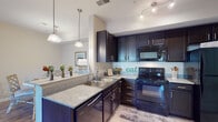 This thoughtfully designed single-floor residence offers a comfortable and cohesive layout that balances style with everyday functionality. The kitchen is a standout feature, showcasing rich dark espresso cabinetry with brushed nickel hardware, granite-style countertops, a double-basin stainless steel sink, and a full suite of black appliances including a range, built-in microwave, dishwasher, and refrigerator. Pendant lighting and track lighting illuminate the space, while tile flooring adds a clean, practical finish. Adjacent to the kitchen, the dining area features wood-look flooring and pendant lighting, providing a welcoming space for meals. The living room offers crown molding, wood-look flooring, and access to natural light through shuttered windows, creating a bright and refined atmosphere. The bedrooms are carpeted and well-lit with natural light from shuttered windows, with ceiling fans adding comfort. A spacious walk-in closet with wire shelving provides generous storage. The bathrooms are finished with tile flooring, dark vanity cabinetry, and a tub-shower combination. A hallway with wood-look flooring connects the rooms, offering a clean, open flow throughout this well-maintained and move-in-ready residence.