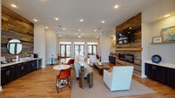 Located at 25 E Revere Blvd in Huntsville, Alabama, this single-story clubhouse serves as a well-appointed community gathering space designed with a warm, contemporary aesthetic. The entry foyer welcomes visitors with tall transom-topped wood-framed glass doors, allowing natural light to flood in while offering views of the surrounding landscaped grounds. A pair of accent chairs flanks the entrance, establishing an inviting first impression.

The main lounge area is defined by warm hardwood flooring throughout and a striking floor-to-ceiling reclaimed wood accent wall that houses a modern linear electric fireplace and a wall-mounted television. Comfortable seating arrangements, including upholstered sofas and accent chairs, create a relaxed social atmosphere, while high ceilings and recessed lighting contribute to a bright and open feel. Multiple sets of French doors along the rear wall provide additional natural light and outdoor views.

Adjacent to the lounge, a wet bar area features dark cabinetry with a white countertop, an under-counter beverage refrigerator, and a sink, all set against a matching reclaimed wood accent wall. A dedicated game room offers a full-size pool table, foosball, bar-height seating, and a wall-mounted television, with oversized windows framing exterior views. Together, these distinct zones create a versatile and engaging communal environment.