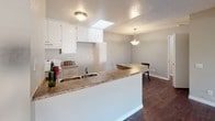 Located at 2600 S Azusa Ave in West Covina, CA, this single-story unit offers a practical and comfortable layout with several notable design features throughout. The kitchen is a functional centerpiece, outfitted with white cabinetry, a granite-style countertop, a built-in electric range, and a double-basin sink. A peninsula breakfast bar opens the kitchen to the dining area, which features rich dark hardwood flooring, a pendant light fixture, and an adjoining skylight that fills the space with natural light. A decorative exposed wood beam defines the transition into the living room, which is carpeted and anchored by a fireplace. Sliding glass doors lead from the living room to a private balcony, offering outdoor access and natural light. The bedrooms are carpeted and feature textured ceilings, with one room equipped with a wall-mounted air conditioning unit and a window with vertical blinds. A generously sized walk-in closet with extensive built-in shelving and hanging rods provides ample storage. The bathroom includes a tub and shower combination with a curtain enclosure. Throughout the unit, neutral tones and textured ceilings contribute to a consistent, understated aesthetic.