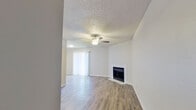 This single-story, one-bedroom, one-bathroom unit offers a thoughtfully organized layout that maximizes its compact footprint. The living room serves as the centerpiece of the home, highlighted by a classic fireplace with a white surround, a ceiling fan with integrated lighting, and a textured ceiling. Wood-look laminate flooring runs throughout, providing a cohesive and low-maintenance aesthetic. A sliding glass door dressed with vertical blinds fills the living area with natural light and offers access to the outdoors.

The kitchen is efficiently designed with white cabinetry, light countertops, and black appliances including a refrigerator, electric range, and an overhead exhaust hood. Adjacent to the main living areas, a hallway connects to the bedroom and closet, ensuring a functional flow throughout the unit.

The bedroom is a comfortable, well-lit space featuring a ceiling fan, a window with natural light, and the same wood-look flooring found throughout the home. A dedicated closet provides practical storage.

The bathroom is clean and straightforward, equipped with a single-sink vanity with light countertops, white cabinetry, a full tub-shower combination with tiled surround, and wood-look flooring. The neutral, light color palette used throughout the entire unit creates a bright and welcoming atmosphere.