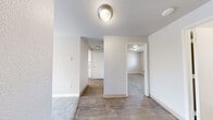 Located at 3701 S Orchard St in Tacoma, Washington, this one-bedroom, one-bathroom unit offers a well-organized, single-floor layout with a clean, neutral aesthetic throughout. The living room serves as the heart of the space, featuring soft gray carpeting, a classic wood-burning fireplace with a tile hearth, and a baseboard heating system. Natural light filters through the windows, lending a bright, airy feel to the room.

The kitchen is efficiently designed with white shaker-style cabinetry, gray countertops, warm wood-look vinyl flooring, and a full suite of white appliances including a refrigerator, range, and dishwasher. An overhead light fixture provides ample illumination, and a hallway connects the kitchen to the rest of the unit.

The bedroom is a quiet, comfortable retreat with plush gray carpeting, a window overlooking the outdoors, and a baseboard heater. A closet is accessible via the connecting hallway, which links the main living areas to the private quarters of the unit.

The bathroom is clean and functional, featuring wood-look vinyl flooring that complements the kitchen, a combined tub and shower with white surrounds, and a vanity with a granite-style countertop. Brushed nickel fixtures add a modern touch throughout. The overall ambiance is calm, bright, and move-in ready.
