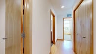 This thoughtfully designed 2-bedroom, 2-bathroom single-floor residence offers a functional and stylish layout that maximizes every square foot. The combined kitchen and living area serves as the heart of the home, showcasing a standout kitchen equipped with rich wood cabinetry, bold granite countertops on both the island and perimeter, and a full suite of stainless steel appliances. Pendant lighting and a large window bathe the space in natural light while framing views of the surrounding landscape. Light hardwood flooring runs throughout the main living areas, complemented by warm wood door trim that lends a cohesive aesthetic throughout. The primary bedroom features plush carpeting, a built-in closet with shelving, and generous window exposure. Both bathrooms are fitted with warm wood vanities, white countertops, large mirrors, and glass-enclosed shower stalls. A dedicated laundry room accommodates a full-size washer and dryer with overhead shelving for added convenience. The hallway connects each space efficiently, maintaining a clean, open flow. Floor-to-ceiling sliding glass doors in the living area open to a balcony with sweeping outdoor views, filling the interior with abundant natural light and a bright, airy ambiance throughout.