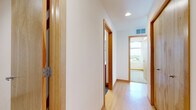 This thoughtfully designed 2-bedroom, 2-bathroom single-floor residence offers a functional and stylish layout that maximizes every square foot. The combined kitchen and living area serves as the heart of the home, showcasing a standout kitchen equipped with rich wood cabinetry, bold granite countertops on both the island and perimeter, and a full suite of stainless steel appliances. Pendant lighting and a large window bathe the space in natural light while framing views of the surrounding landscape. Light hardwood flooring runs throughout the main living areas, complemented by warm wood door trim that lends a cohesive aesthetic throughout. The primary bedroom features plush carpeting, a built-in closet with shelving, and generous window exposure. Both bathrooms are fitted with warm wood vanities, white countertops, large mirrors, and glass-enclosed shower stalls. A dedicated laundry room accommodates a full-size washer and dryer with overhead shelving for added convenience. The hallway connects each space efficiently, maintaining a clean, open flow. Floor-to-ceiling sliding glass doors in the living area open to a balcony with sweeping outdoor views, filling the interior with abundant natural light and a bright, airy ambiance throughout.