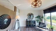 Located at 2727 E 86th St in Indianapolis, Indiana, this contemporary single-floor residence showcases a thoughtfully designed open-concept layout with high-end finishes throughout. Rich hardwood-style flooring flows seamlessly across the main living areas, anchoring a cohesive and modern aesthetic.

The living area is bright and inviting, featuring a striking copper-toned cage chandelier, an industrial-style glass-front cabinet, and large floor-to-ceiling sliding glass doors that frame sweeping outdoor views of the surrounding greenery. Natural light floods the space, enhancing its open and airy atmosphere.

The kitchen is well-appointed with dark espresso cabinetry, granite countertops, a stainless steel appliance suite, and a decorative wine rack. A generously sized granite island with seating for multiple guests serves as both a functional workspace and a casual dining hub, illuminated by pendant lighting overhead.

The bedroom offers a serene retreat, complete with plush carpeting, a ceiling fan, a tufted upholstered headboard, and transom-style windows that allow soft, diffused light. The space also features access to walk-in closet storage.

The bathroom is elegantly finished with a dark-framed vanity mirror, granite countertops, dark cabinetry, and a glass-enclosed walk-in shower with slate tile surround, delivering a spa-like experience.