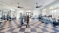 Located in Santa Rosa Beach, FL, this fitness center offers a generously sized, single-floor exercise space designed to support a full range of workout routines. The interior is defined by soaring ceilings fitted with large, multi-blade ceiling fans that ensure effective air circulation throughout. A classic checkerboard-patterned floor in neutral tones anchors the room with a clean, polished aesthetic.

Natural light pours in through an array of large, white-framed windows lining multiple walls, providing bright, airy views of the surrounding greenery. Floor-to-ceiling mirrors are strategically positioned to visually expand the space while allowing users to monitor their form during workouts.

The cardio section is well-appointed with treadmills, elliptical trainers, and stationary bikes arranged along the windowed perimeter. The strength training area features professional-grade cable and pulley machines, multi-function Smith machines, and a full dumbbell rack. A dedicated entryway with warm hardwood flooring and nautical-themed framed artwork provides a welcoming transition into the facility.

Recessed lighting complements the natural daylight, ensuring the space remains well-lit at all hours. The overall ambiance is clean, modern, and functional — an ideal fitness environment for residents of the Santa Rosa Beach community.