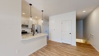 Located at 504 East Geesee Pointe Drive in West Henrietta, NY, this single-floor home offers five bedrooms and two bathrooms within a thoughtfully designed layout. The open-concept kitchen and living area serves as the heart of the home, featuring light hardwood-style flooring, recessed lighting, and two pendant lights that hang above a white quartz peninsula with an undermount sink. The kitchen is equipped with stainless steel appliances, including a range, microwave, and side-by-side refrigerator, complemented by gray shaker-style cabinetry extending to the ceiling. The living area receives generous natural light through a sliding glass door that opens to an outdoor balcony with views of a natural wooded area and a small pond. The bedrooms are carpeted and bright, with large windows that invite abundant sunlight; the primary bedroom includes a walk-in closet. The bathrooms feature white cabinetry with black hardware accents, quartz countertops, and hardwood-style flooring. Clean white walls and a neutral color palette throughout lend the home a modern, cohesive aesthetic.