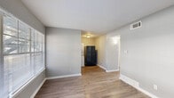 This two-bedroom, one-bathroom unit in Memphis, Tennessee offers a straightforward and functional layout across a single floor. The interior is finished with wood-style plank flooring throughout and neutral gray walls, creating a clean, cohesive aesthetic from room to room. The living area provides an open feel, with a window allowing natural light to fill the space, and flows directly into the kitchen. The kitchen is equipped with a gas range, black refrigerator, and gray cabinetry, and notably includes a stacked washer and dryer unit, adding significant in-unit convenience. Both bedrooms feature the same wood-style flooring and gray wall tones, with windows fitted with horizontal blinds providing natural light and privacy. The primary bedroom is a comfortable size and includes closet access. The second bedroom is more compact but similarly appointed. The full bathroom features a tub-shower combo with white subway tile surround, complemented by gray walls for a clean, functional finish. A hallway connects the main areas of the home, and a dedicated closet provides additional storage. White trim and baseboards throughout add a crisp contrast to the gray walls, contributing to the unit's tidy, well-maintained appearance.