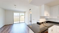This compact yet efficiently designed 1-bedroom, 1-bathroom unit offers a thoughtful single-floor layout that maximizes every square foot. The open-concept kitchen and living area forms the heart of the space, where warm hardwood-style flooring flows throughout, complemented by bright white walls that enhance the sense of openness. A sliding glass door leads to a private balcony, flooding the living area with natural light and providing pleasant outdoor views of the surrounding neighborhood.

The kitchen is well-equipped, featuring dark granite countertops that contrast smartly against white shaker-style cabinetry extending to the ceiling for ample storage. Black appliances — including a gas range, over-the-range microwave, and a full-size refrigerator — provide a modern, cohesive look. Track lighting overhead ensures the kitchen is well-lit for cooking and entertaining.

The bedroom is a calm, minimalist retreat with clean white walls, hardwood-style flooring, track lighting, and a sliding closet for storage. A dedicated closet space adds to the unit's organizational functionality.

The bathroom features a full tub-shower combination with white tile surround and polished chrome fixtures, offering a clean and functional design. A hallway connects the rooms, contributing to a logical and private flow throughout the unit.