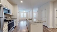 Located at 1226 Bexton St in Charlotte, NC, this single-floor unit offers a clean, contemporary design with an open and functional layout. The kitchen serves as the heart of the space, anchored by a large central island with granite countertops and an integrated sink. White cabinetry with sleek hardware lines the walls, complemented by a grey tile backsplash and a full suite of stainless steel appliances, including a refrigerator, range, and microwave. Wood-style flooring runs throughout, adding warmth and visual continuity across all areas. The open-concept design connects the kitchen seamlessly to a bright and airy living area, which benefits from multiple windows fitted with blinds that allow for ample natural light. Ceiling fans in the living area provide both comfort and a polished finish. The bedroom is generously sized with a ceiling fan, wood-style floors, and direct access to a well-appointed walk-in closet. The bathroom features a granite-topped vanity with under-sink cabinetry, a full tub-shower combination, and consistent wood-style flooring. Recessed lighting throughout the unit contributes to a bright, modern atmosphere. The overall design reflects a cohesive, neutral palette well-suited for comfortable everyday living.