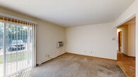 This single-floor, 2-bedroom, 1-bathroom unit offers a practical and efficient layout designed to maximize everyday comfort. Soft carpet flooring runs throughout the living areas and bedrooms, complemented by neutral cream-toned walls that create a clean, understated aesthetic. The living room is a comfortable, open space equipped with a wall-mounted air conditioning unit and baseboard heating, and features a sliding glass door that invites natural light and outdoor views. The kitchen is well-appointed with warm oak cabinetry, dark countertops, a double-basin sink, and tile flooring, with an adjacent pantry providing additional storage. A separate dining area connects smoothly to the kitchen and living spaces for a cohesive flow. The two bedrooms are carpeted and bright; the primary bedroom benefits from generous natural light through a wood-framed window and features two side-by-side sliding closet doors for ample storage. The second bedroom offers its own closet and baseboard heating. The bathroom is finished with large-format beige tile work extending from the floor through the tub surround, paired with a wood-framed vanity mirror and a clean white soaking tub. With five closets total throughout the unit, storage is a notable strength of this thoughtfully laid-out space.