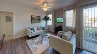 This single-story residence is thoughtfully designed with a cohesive aesthetic carried throughout each room. An arched entryway hallway provides a welcoming transition into the main living area, where rich wood-look flooring, a ceiling fan, and multiple windows with blinds create a bright, comfortable atmosphere. The living room offers generous seating space and natural light from multiple windows flanking the walls.

The kitchen features white shaker-style cabinetry, grey quartz-style countertops, and a full suite of stainless steel appliances, including a range, microwave, dishwasher, and refrigerator. Wood-look flooring continues here, enhancing the clean, modern feel.

Adjacent to the living area, the dining space includes a sliding glass door with vertical blinds that opens to an outdoor view, filling the room with natural light.

The bedrooms are carpeted and well-sized, offering ample room for furniture. The primary bedroom includes a walk-in closet and an en-suite bathroom. Both bathrooms feature white cabinetry, grey countertops, tub-shower combinations, and wood-look flooring, maintaining a uniform, polished look throughout the home.
