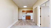 This single-floor unit at 1551 Bryden Rd in Columbus, Ohio offers a practical and straightforward layout. The kitchen is equipped with warm-toned wood cabinetry, a granite-patterned countertop with a stainless steel sink, a white electric range, and a refrigerator, all set beneath a drop-panel ceiling with recessed lighting. Light wood-look vinyl flooring runs through the kitchen and extends into adjoining areas, creating a cohesive flow. The main living area transitions to plush carpeting, providing a softer underfoot feel, and features neutral cream-toned walls that lend a clean, open atmosphere. Visible conduit runs along the upper wall, reflecting a utilitarian design aesthetic. The bedroom area is generously appointed with multiple closet spaces, including open wire shelving units and a sliding-door closet with a wood overhead shelf, offering ample storage. The bathroom is cleanly finished with wood-look vinyl flooring, a full tub and shower combination equipped with grab bars for accessibility, a toilet, and a vanity. The overall ambiance of the unit is simple, functional, and well-maintained, suited for comfortable everyday living.