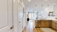 This thoughtfully designed one-bedroom, one-bathroom residence offers an efficient and stylish single-floor layout. The open-concept living and kitchen area serves as the heart of the home, where warm hardwood-style flooring flows throughout. The kitchen is a standout feature, equipped with stainless steel appliances including a refrigerator, range, microwave, and dishwasher. Two-toned cabinetry pairs natural wood lower cabinets with crisp white uppers, complemented by a white quartz countertop, subway tile backsplash, and a central island with seating for three. Sleek pendant lights hang above the island, adding a modern touch. The living area benefits from large French doors that invite generous natural light and open views. A ceiling fan keeps the space comfortable year-round. The bedroom is a serene retreat featuring plush carpet, a ceiling fan, and a large window with an outdoor view. It also provides access to a spacious walk-in closet outfitted with dual hanging rods and built-in shelving. The bathroom features a full-length vanity with ample storage, a large mirror, and a soaking tub with tiled surround. Clean white walls and neutral finishes throughout create a bright, cohesive ambiance.