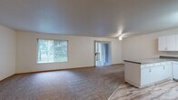 Located at 1616 NE 16th Way in Gresham, Oregon, this single-floor residence offers a clean, functional layout with comfortable living spaces throughout. The expansive living room is a standout feature, with plush carpeting, neutral white walls, and abundant natural light streaming in through a large picture window and a sliding glass door fitted with vertical blinds. A ceiling fan adds comfort, while the sliding door provides direct access to the outdoors and views of surrounding greenery. The kitchen is well-equipped with white cabinetry offering ample storage, dark laminate countertops, a double sink, a white electric range, a dishwasher, and light wood-look flooring that adds warmth to the space. A breakfast bar-style peninsula separates the kitchen from the adjoining areas. The bedrooms are carpeted and offer natural light through vertical-blind windows, with at least one bedroom featuring a sliding wood-door closet with built-in shelving. The bathrooms include light wood-look flooring, white vanity cabinetry with neutral countertops, wall mirrors, and grab bars. One bathroom includes a full tub and shower combination. Overall, the space presents a tidy, practical design suited for comfortable everyday living.