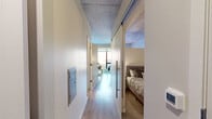 Located on the sixth floor at 814 Portland Ave in Minneapolis, MN, this one-bedroom, one-bathroom unit offers a well-designed layout across a single floor. The galley-style kitchen is a standout feature, equipped with stainless steel appliances including an electric range with oven, over-the-range microwave, and dishwasher. Crisp white cabinetry, a subway tile backsplash, and a light stone countertop complement the space, while large floor-to-ceiling windows flood the kitchen with natural light and frame striking views of the Minneapolis skyline. Light hardwood flooring extends through the main living areas, enhancing the bright, contemporary feel. A built-in bar-height counter along the window provides additional dining or workspace. The bedroom is generously proportioned, featuring soft carpet, neutral warm-toned walls, an exposed concrete ceiling detail, and a sleek sliding barn-style door that leads to the closet. The bathroom is thoughtfully appointed with a full tub-shower combo featuring tile surround, a white vanity with ample cabinet storage, a large mirror, and warm wood-tone flooring. A hallway and dedicated closet complete the functional layout of this modern urban residence.