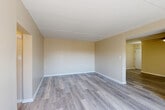 This single-floor unit in Philadelphia, PA is thoughtfully laid out to maximize functionality across its well-defined living spaces. The entrance leads into an open area connecting the kitchen, dining room, and living room, creating a cohesive and practical flow throughout the home. The kitchen features light wood cabinetry, a tile backsplash, a peninsula counter for additional prep or dining space, and black appliances including a gas range, microwave, and refrigerator. Tile flooring in the kitchen transitions to durable laminate wood-style flooring throughout the main living areas, which are brightened by natural light from multiple windows. The dining room and living room offer open, airy spaces with neutral warm-toned walls and clean white baseboards. The bedroom is carpeted for comfort and includes a sliding-door closet, a second closet for additional storage, and a window with an outdoor view of surrounding brick architecture. The bathroom is finished with white wall tile and a decorative mosaic accent border above the tub-shower combination. A hallway connects the private and shared spaces, completing this efficient and well-appointed home.