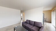 Located at 1930 S Goyer Rd in Kokomo, Indiana, this single-floor unit offers three bedrooms, one bathroom, and a living room connected by a central hallway. The living room serves as the heart of the space, featuring light wood-look flooring, clean white walls, and a wide window fitted with blinds that invites natural light. A wall-mounted HVAC unit and baseboard heating provide climate control throughout. The room offers ample space for seating and entertainment, with a TV area accented by modern wall art. The three bedrooms maintain the same consistent flooring and neutral palette. The primary bedroom includes a closet with built-in shelving and hanging rods, while each bedroom features a window for natural light and ventilation. The bathroom is efficiently designed with a full tub-and-shower combination, a toilet, and wood-look flooring. A hallway connects the bedrooms to the main living area and bathroom, creating a logical and accessible flow. Throughout the unit, the clean, minimalist aesthetic and consistent use of light tones create a bright and functional living environment suited for everyday comfort.