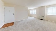 This 1-bedroom, 1-bathroom residence is designed with a straightforward, single-floor layout that maximizes functionality and ease of living. The living area is generously sized, featuring neutral-toned wall-to-wall carpeting and warm beige walls that create a clean, open atmosphere. Multiple windows fitted with horizontal blinds allow natural light to filter in, brightening the space throughout the day. An arched doorway adds a subtle architectural detail, connecting the living area to the rest of the unit. The kitchen is a standout feature, outfitted with rich dark wood cabinetry, dark granite-style countertops, and warm hardwood-style flooring. Black appliances — including a refrigerator, gas range, dishwasher, and microwave — provide a cohesive, functional aesthetic. Ample cabinet storage and counter space make this kitchen well-suited for everyday cooking. The bathroom is finished with floor-to-ceiling neutral tile surrounding a full soaking tub and shower combination, complemented by clean white fixtures and classic tile flooring. The bedroom offers a comfortable, carpeted retreat consistent with the overall neutral palette of the home. Together, the rooms form a cohesive, livable space with a clean and understated design throughout.