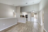 Located at 11000 Point Sylvan Circle in Orlando, FL, this 2-bedroom, 2-bathroom home offers a well-designed single-level layout with modern finishes throughout. The open-concept living, dining, and kitchen area forms the heart of the home, featuring soaring vaulted ceilings with pendant lighting, light wood-look flooring, and a neutral warm-gray color palette that creates a bright and cohesive atmosphere. A half-wall with a breakfast bar separates the kitchen, which is equipped with stainless steel appliances including a refrigerator, range, and microwave, complemented by white cabinetry and granite-style countertops. A convenient in-unit laundry area is tucked just off the kitchen. The primary bedroom is a standout feature, boasting a vaulted ceiling, an arched window that floods the room with natural light, views of lush greenery, a ceiling fan, and a spacious walk-in closet with wire shelving. The second bedroom is also well-proportioned with a ceiling fan and a window overlooking the outdoors. Both bathrooms offer consistent finishes with white vanities, tub-shower combinations, and wood-look tile flooring. Additional storage is provided by multiple closets, and a den adds flexible living space. The home also includes a staircase, suggesting access to an entry or utility area below.